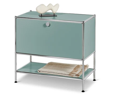 Türkisfarbener Schrank mit Chromrahmen, darauf eine weiße Dekoration, darunter eine Decke.
