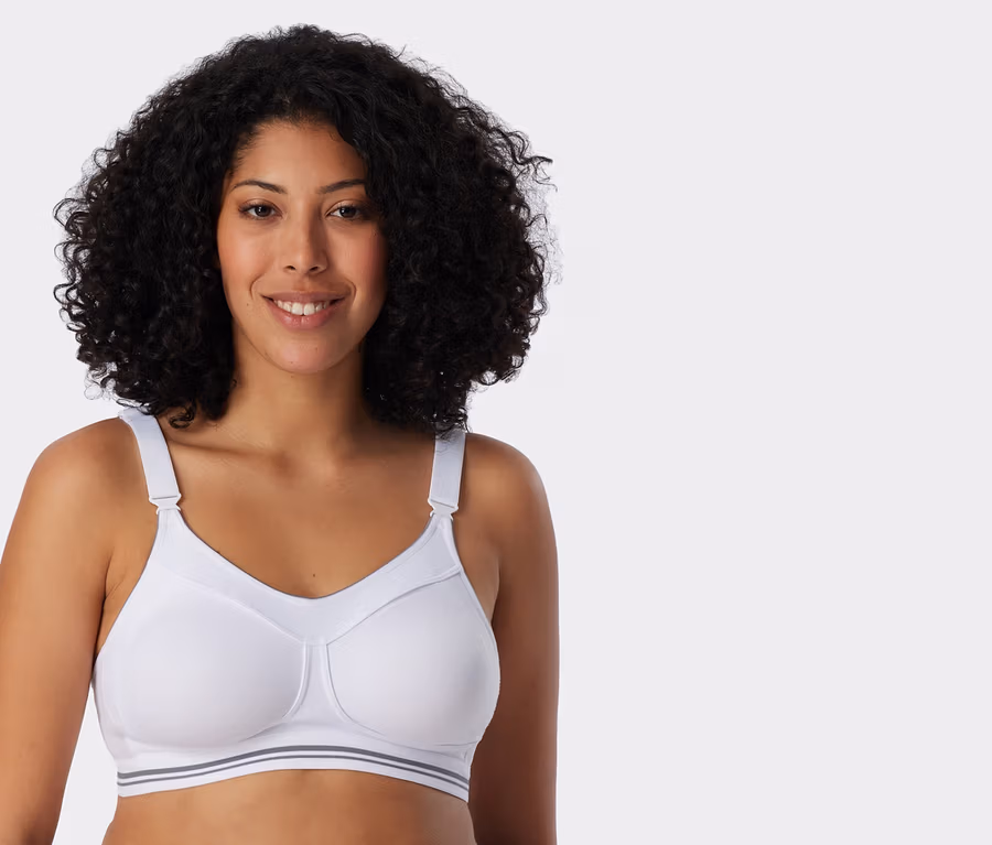 Lächelnde Frau mit lockigem Haar trägt einen weißen SCHIESSER High Impact Sport-BH mit grauen Streifen am Bund.