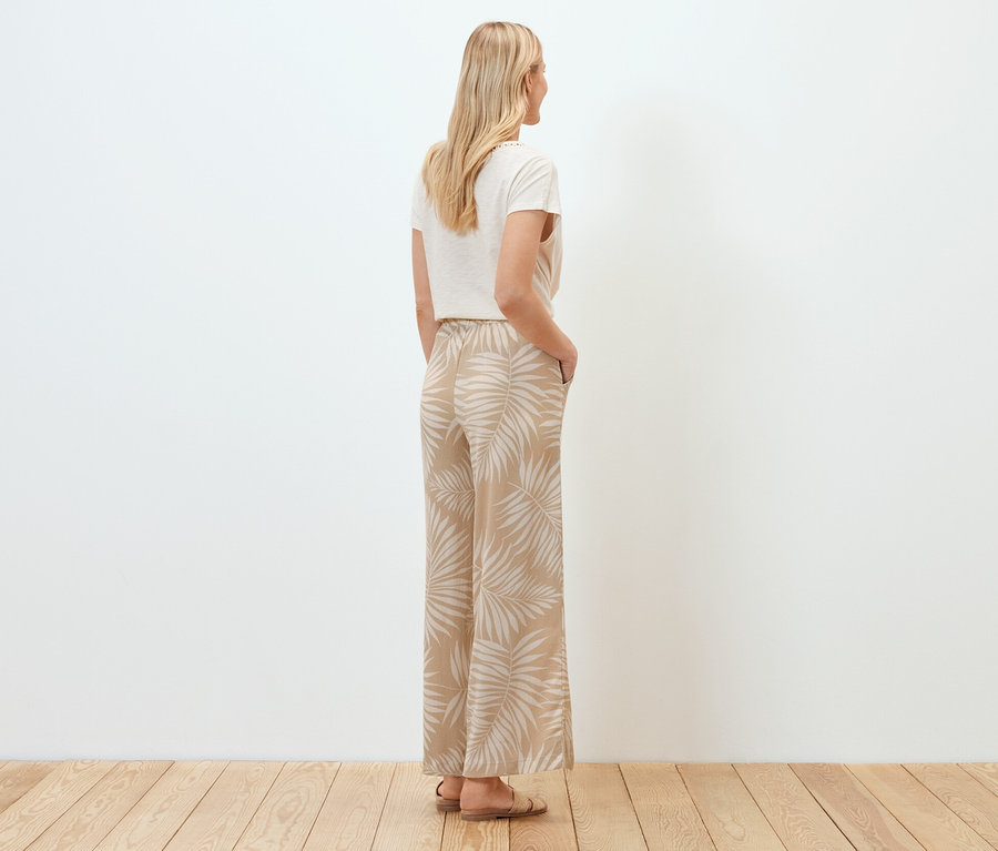 Frau steht mit dem Rücken zur Kamera und trägt eine strukturierte Palazzohose mit Alloverprint.