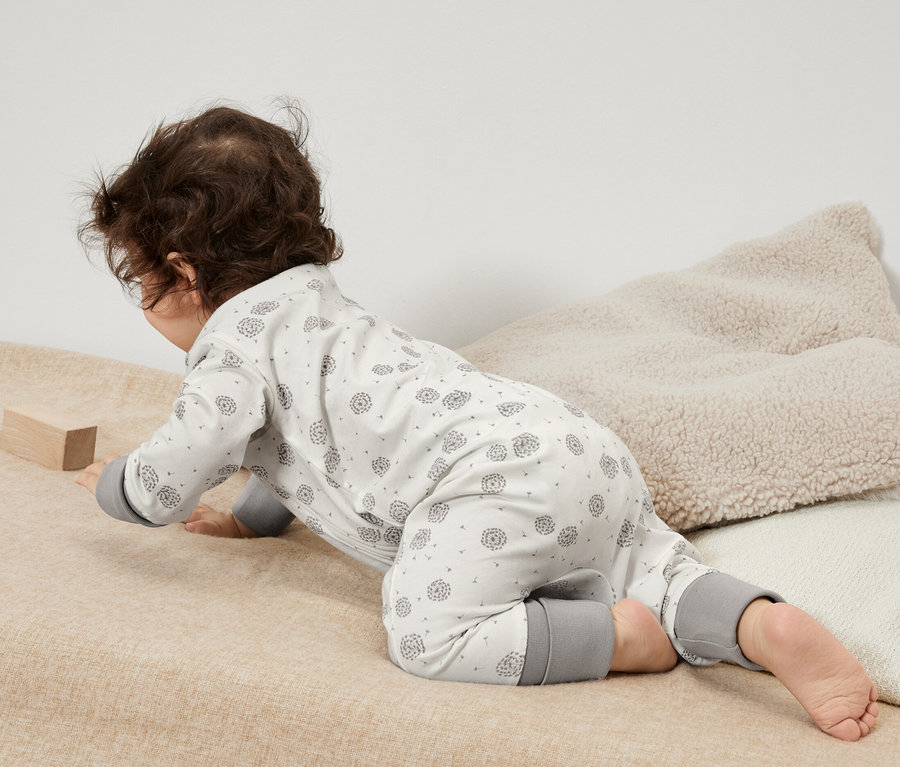 Ein Baby krabbelt auf einer beigen Decke in einem 3er-Pack Baby-Pyjamas mit grauen Details und spielt mit einem Holzklotz.
