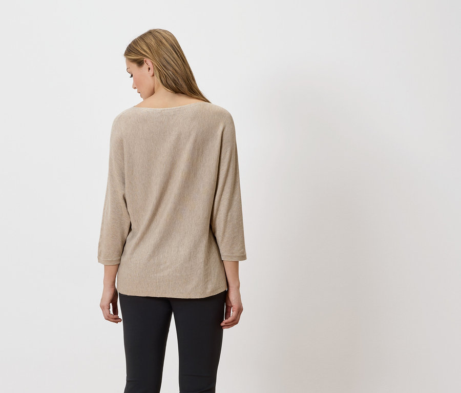 Rückansicht einer Frau mit blonden Haaren, die einen beigefarbenen Pullover und schwarze Hosen trägt.