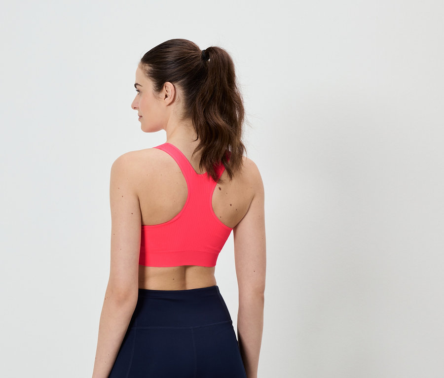 Rückansicht einer Frau mit Pferdeschwanz, die einen pinken Sport-BH und marineblaue Leggings trägt.