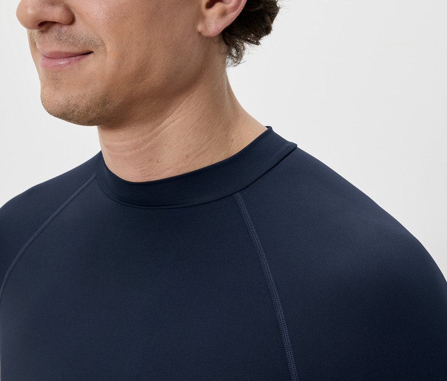 Nahaufnahme eines Mannes mit dunklem, langärmligem Shirt vor einem hellen Hintergrund.