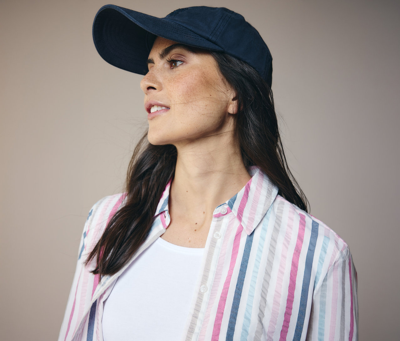 Frau mit dunkelblauer Kappe und gestreifter CECIL Hemdbluse. Sie blickt nach links.
