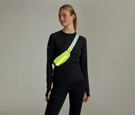 Frau mit Pferdeschwanz, schwarzem Langarmshirt und Leggings, trägt eine neongelbe Bauchtasche quer über der Brust.