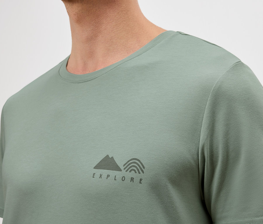 Nahaufnahme eines Mannes, der ein hellgrünes T-Shirt mit einem kleinen "Explore"-Logo trägt.