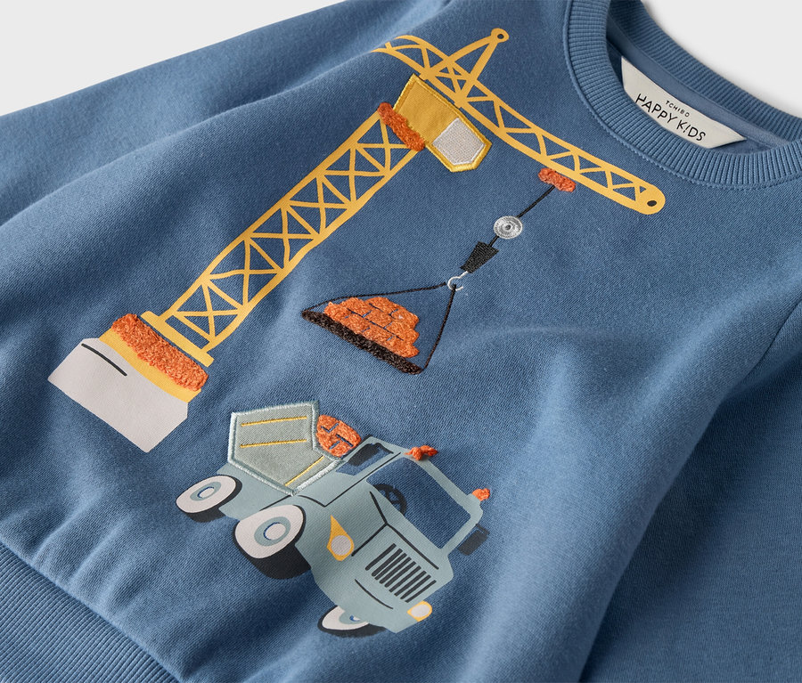 Auf einem blauen Pullover ist ein gelber Kran abgebildet, der über einem Lastwagen mit Rädern steht.