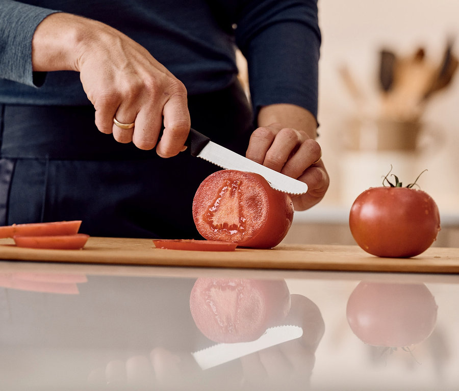 Person schneidet eine Tomate auf einem Holzbrett mit einem Messer.