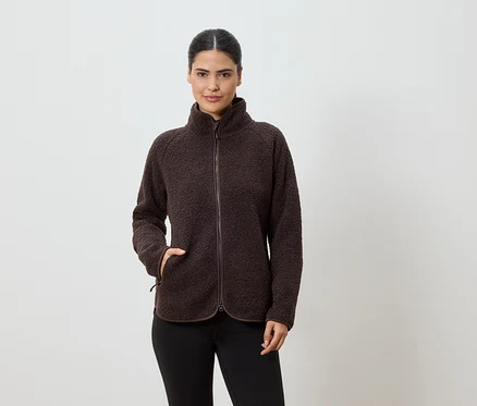 Frau mit Zopf trägt eine braune Fleecejacke mit Reißverschluss und schwarzen Leggings vor einem weißen Hintergrund.