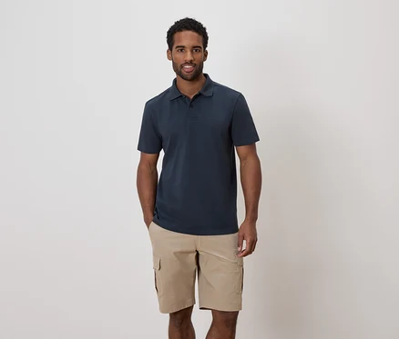 Ein Mann mit dunklen Haaren und Bart trägt ein marineblaues Poloshirt und Khaki-Cargo-Shorts.