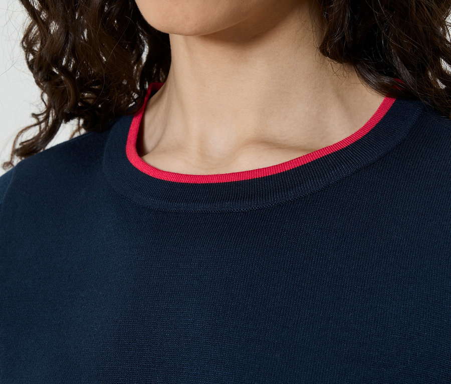 Nahaufnahme einer Frau mit lockigem Haar, die einen dunkelblauen Pullover mit rotem Kragen trägt.