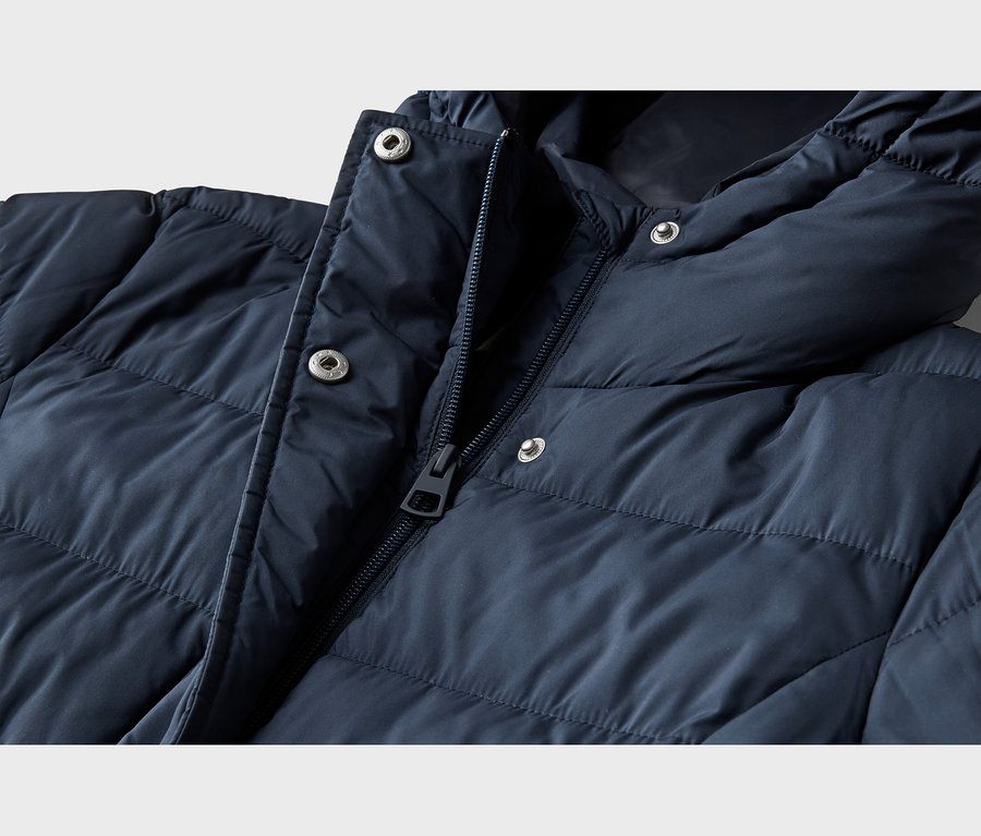Nahaufnahme einer marineblauen Steppjacke. Die Jacke hat einen teilweise geöffneten Reißverschluss, silberne Druckknöpfe an der Knopfleiste und Kapuze sowie ein gestepptes Design.