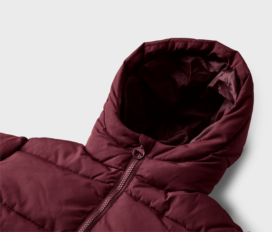 Nahaufnahme einer bordeauxroten Steppjacke, die die gepolsterte Textur, die Kapuze und den passenden Reißverschluss mit rundem Zipper zeigt.