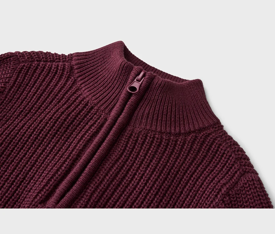 Nahaufnahme eines burgunderroten Strickpullovers mit Rippenstruktur, Reißverschluss und Stehkragen.