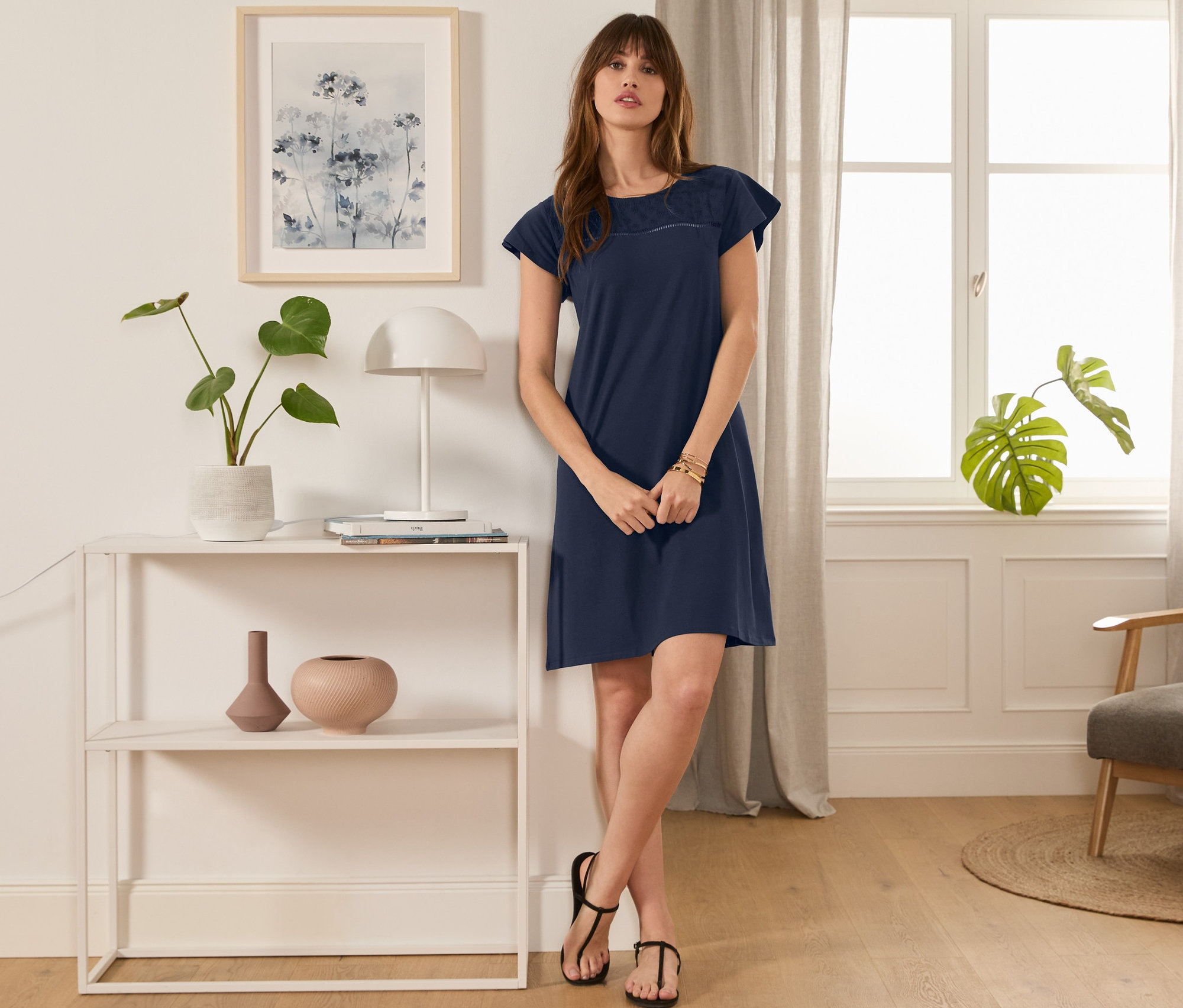 Eine Frau steht in einem Raum und trägt ein dunkelblaues Jerseykleid mit Lochstickerei.