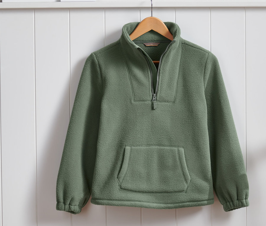 Ein olivgrünes Kuschelfleece-Sweatshirt hängt an einem Holzbügel vor einer weißen Wand mit Holzverkleidung.