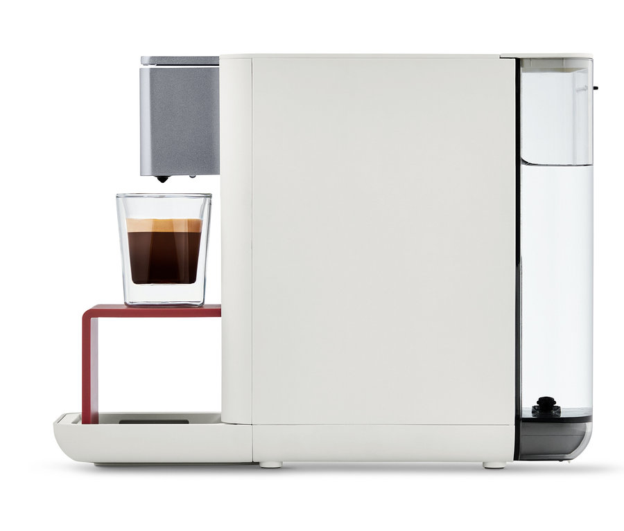 Weiße Qbo ESSENTIAL Bright Coral Kaffeemaschine mit einer Tasse Kaffee.