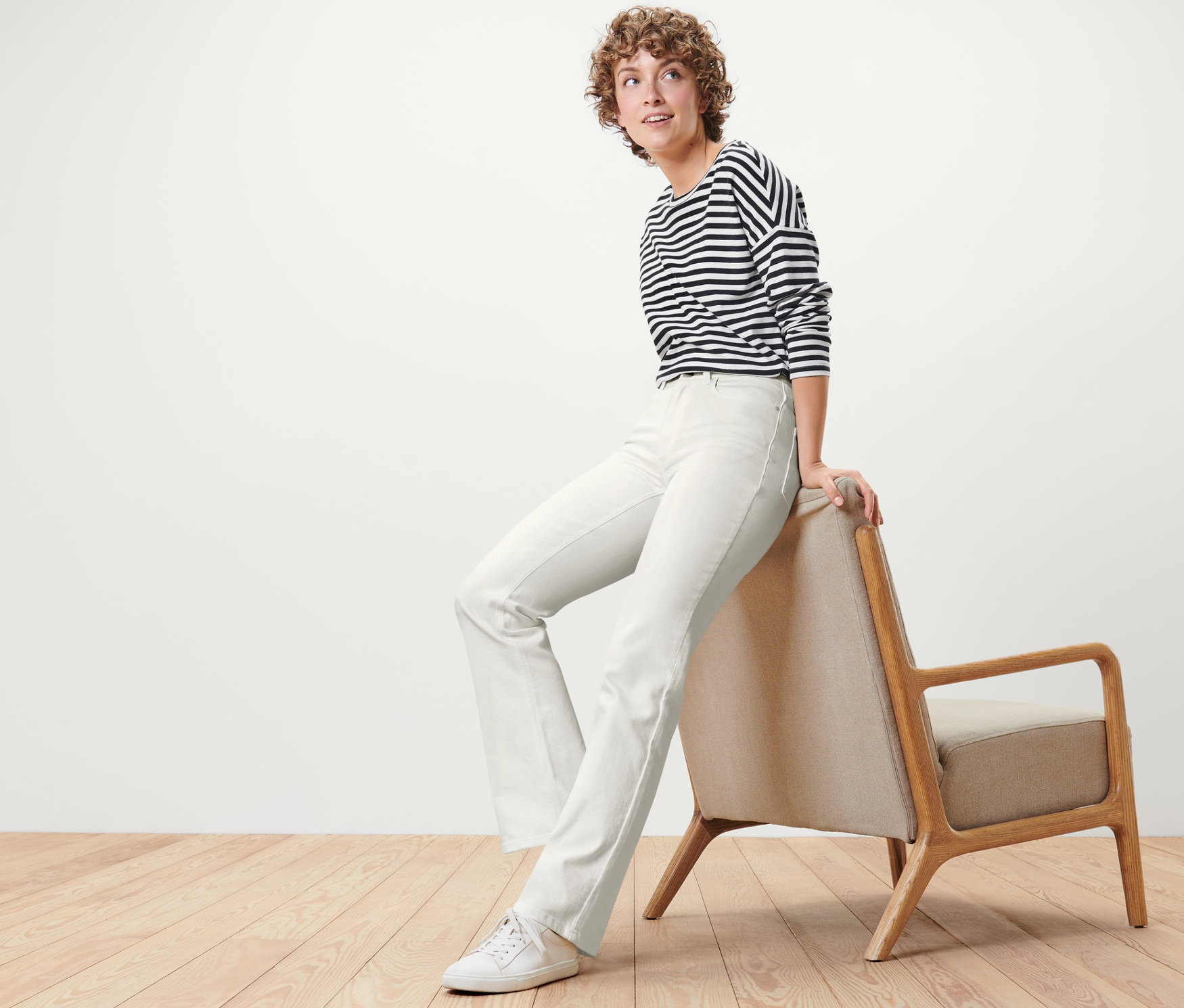Eine Frau sitzt auf einem Sessel und trägt eine cremeweiße Bootcut Jeans – Fit »Lou«.
