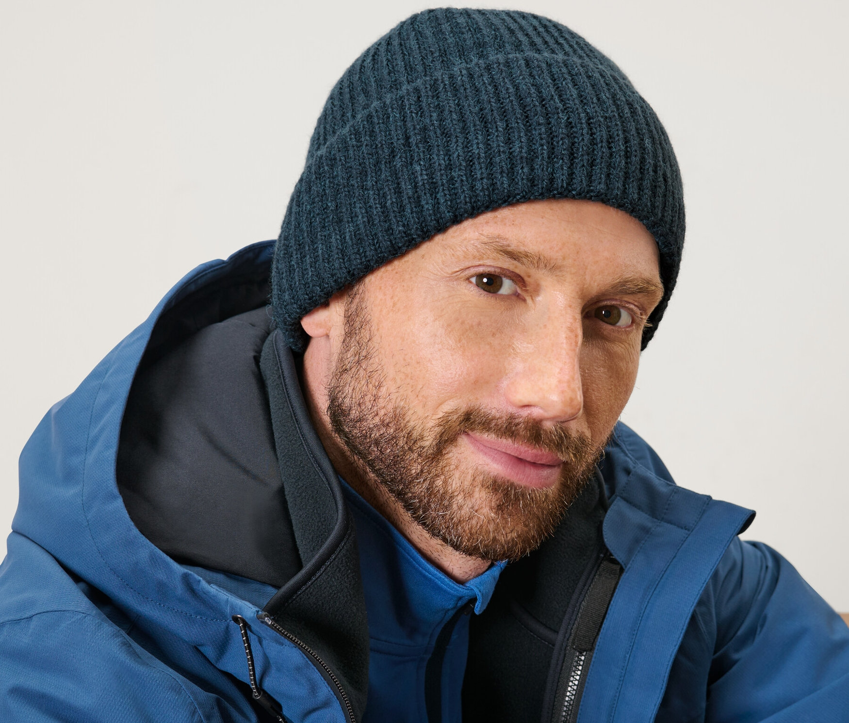 Mann mit Bart trägt eine blaue Strickmütze und eine blaue Jacke.