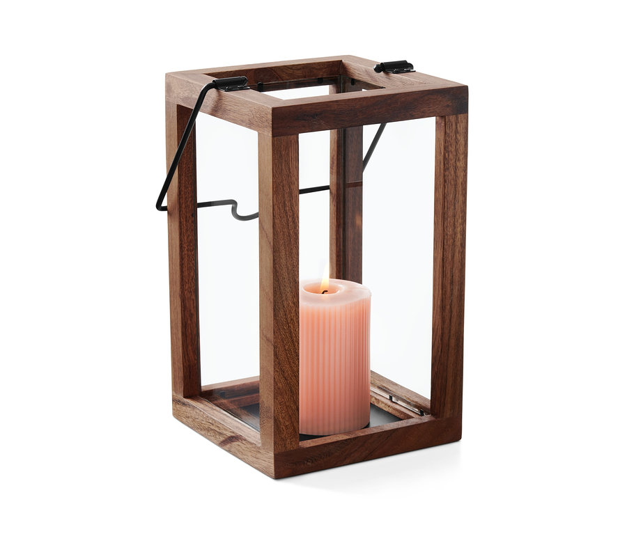 Eine rosa Kerze brennt in einem Windlicht aus Holz und Glas.