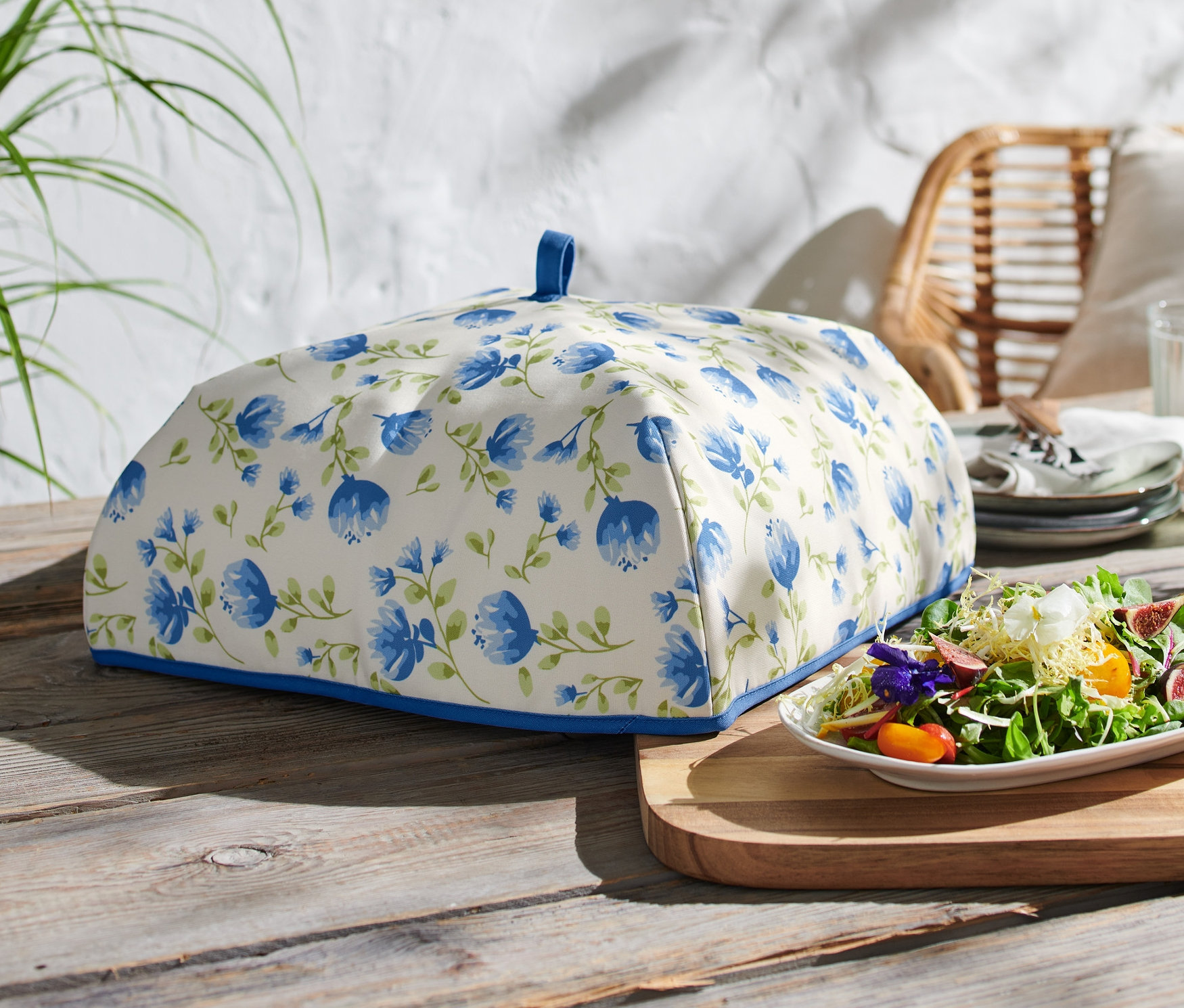 Thermo-Abdeckhaube mit blauen Blumen auf einem Holztisch.