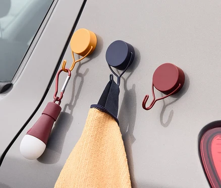 Drei Magnethaken sind an einem grauen Auto befestigt. An einem Haken hängt ein Handtuch, an dem anderen eine Lampe.