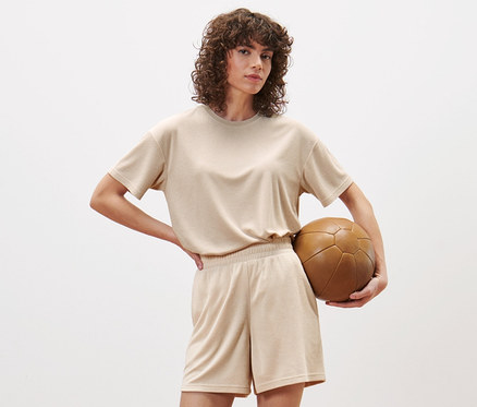 Frau posiert im Studio und trägt Frottier-Sportshorts und hält einen braunen Fußball.