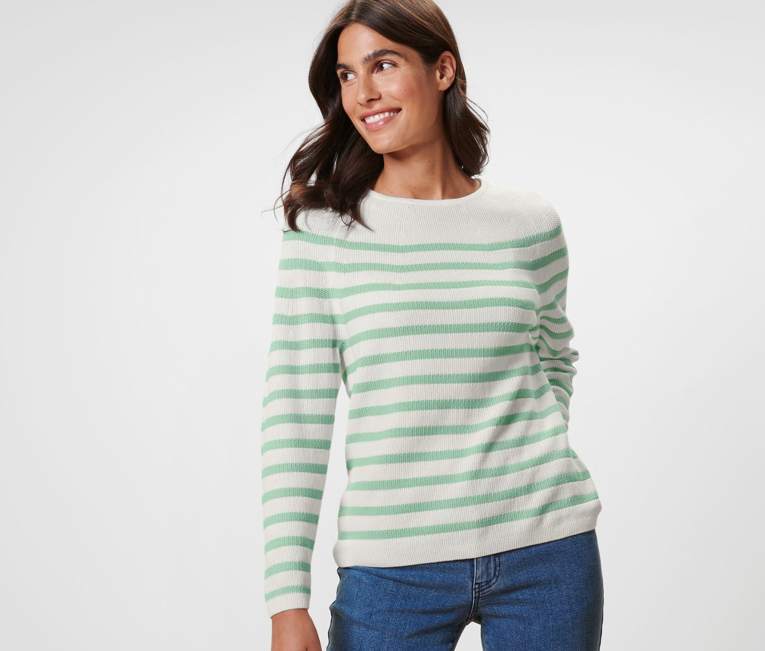 Lächelnde Frau posiert in einem gestreiften Strickpullover und blauen Jeans.