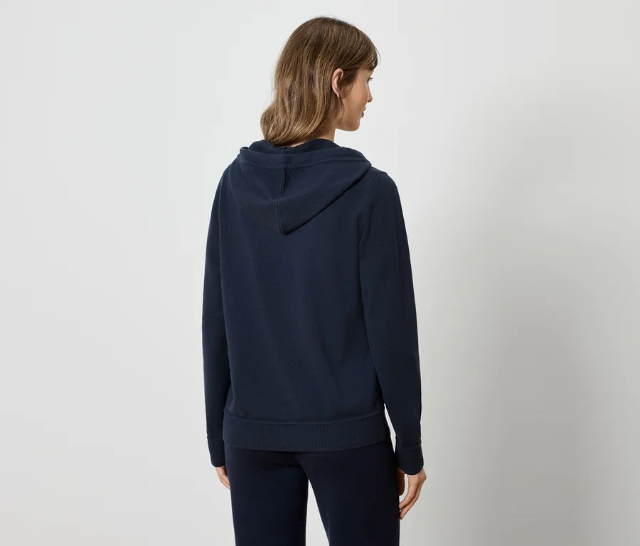 Frau mit dem Rücken zur Kamera trägt einen dunkelblauen Kapuzenpullover und eine Trainingshose.