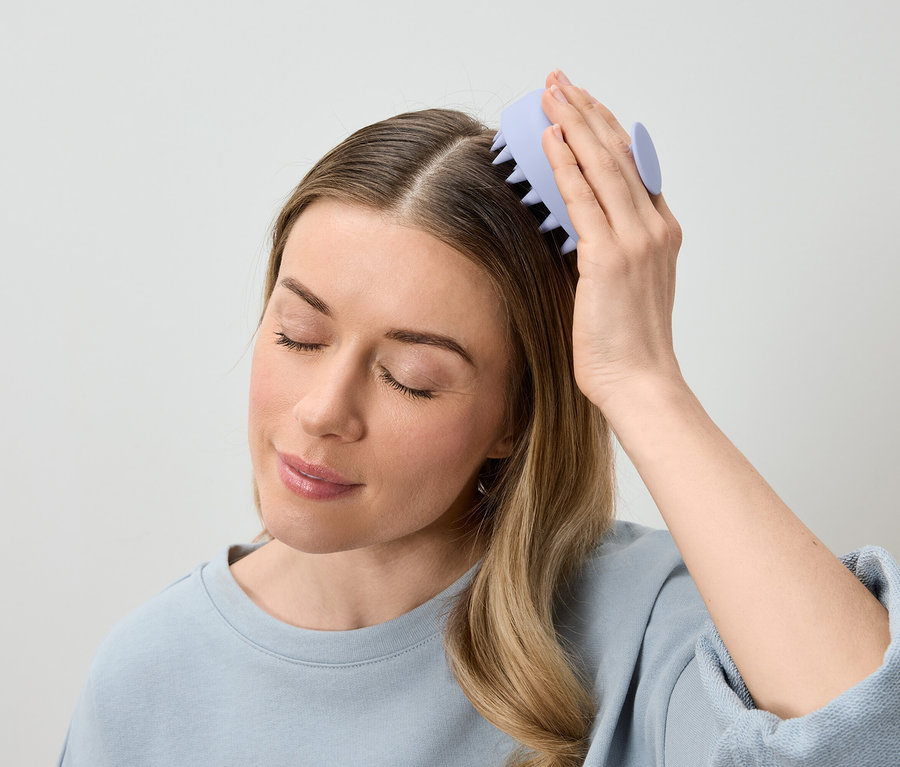 Frau massiert ihre Kopfhaut mit einer hellvioletten Kopfmassagebürste.