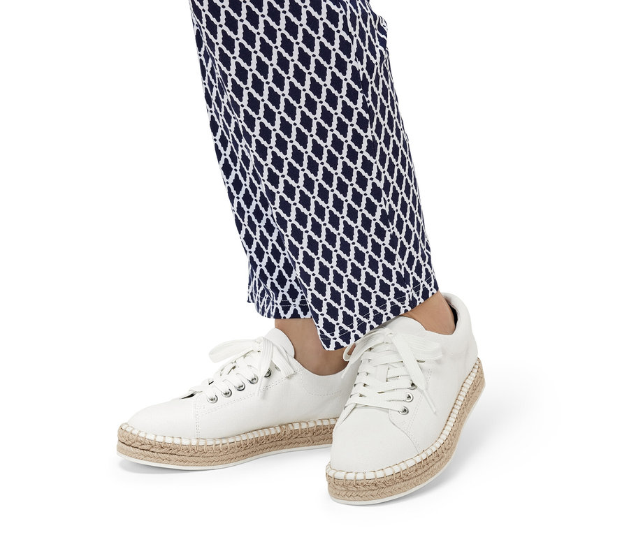 Beine in blau-weiß gemusterter Hose und weißen Canvas-Sneakers.