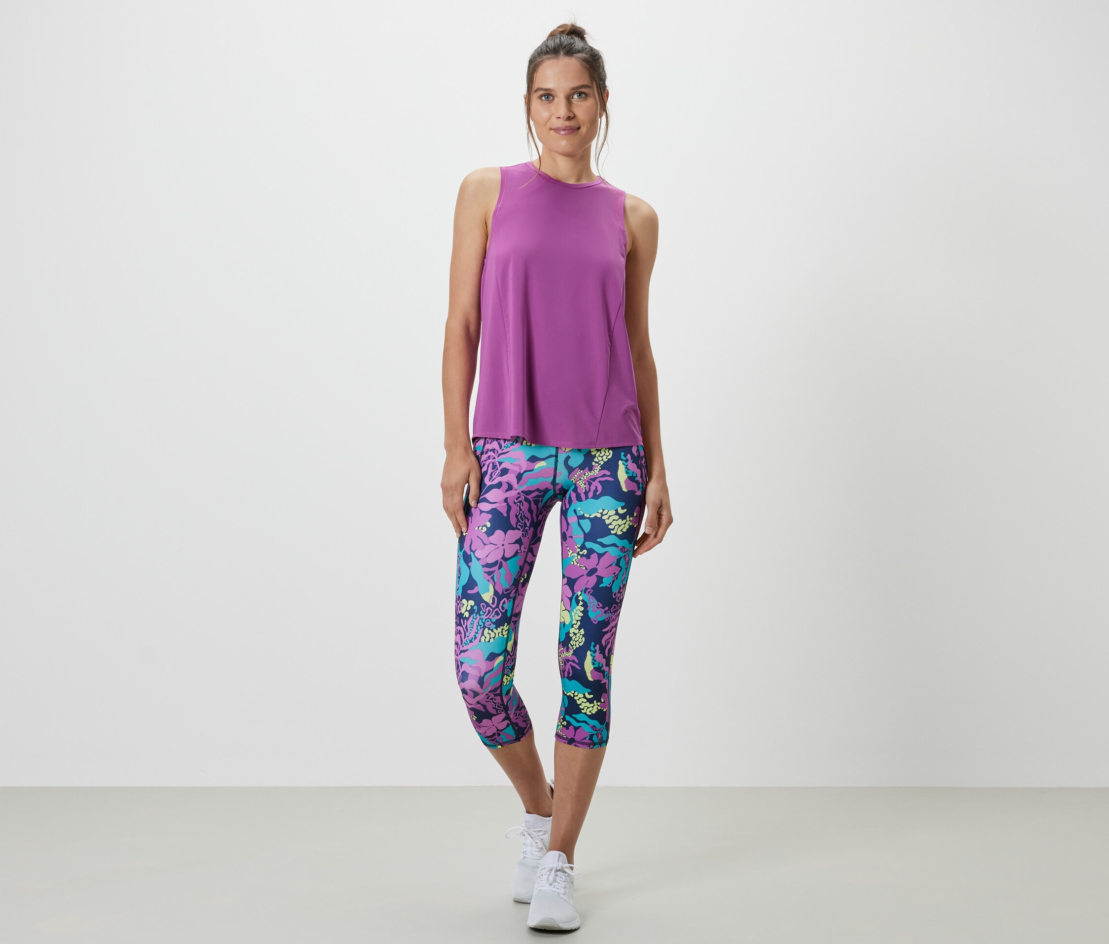 Frau trägt ein türkises Sport-Top aus einem zweiteiligen Set und Leggings mit Blumenmuster.