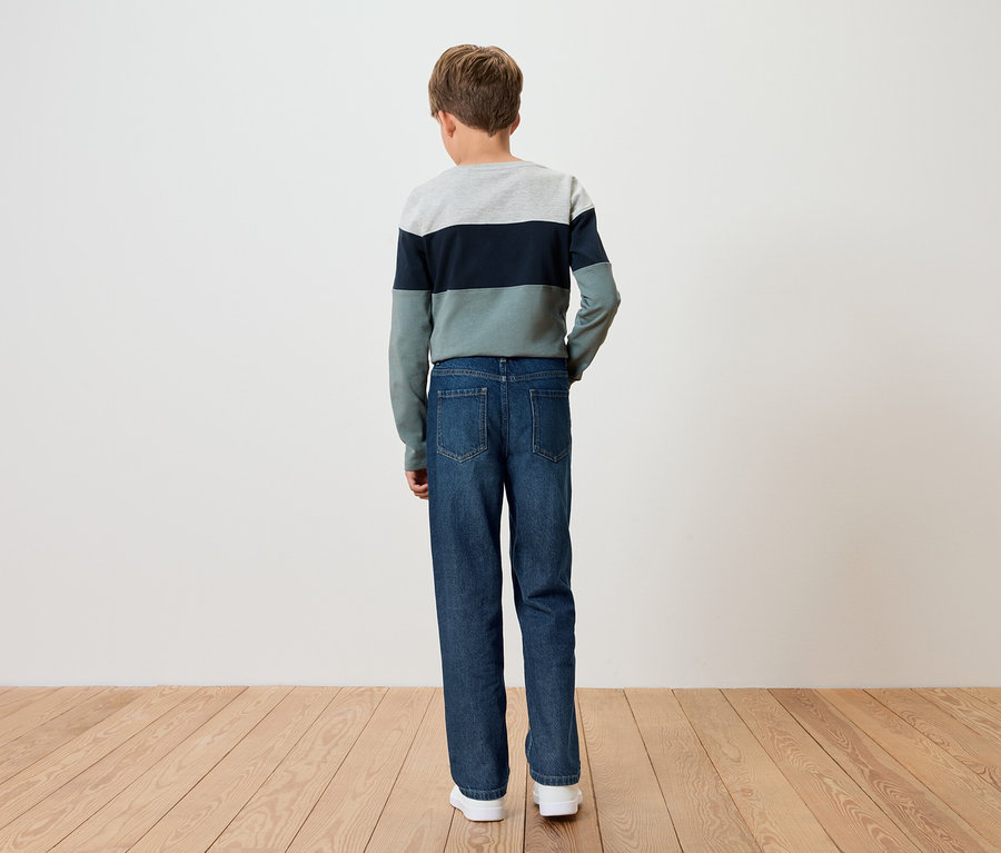 Ein Junge steht mit dem Rücken zur Kamera, er trägt einen gestreiften Pullover und blaue Jeans.