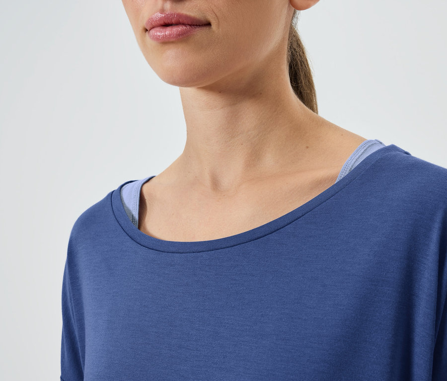 Detailaufnahme einer Frau mit braunen Haaren, die ein blaues Kurzarm-T-Shirt und ein blaues Tanktop trägt.