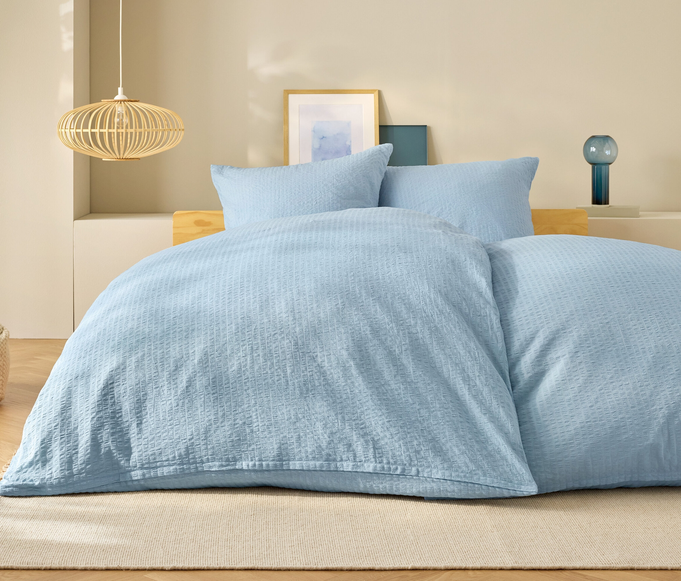 Hellblaue Bettwäsche auf einem Bett mit Kissen und Lampe im Hintergrund.