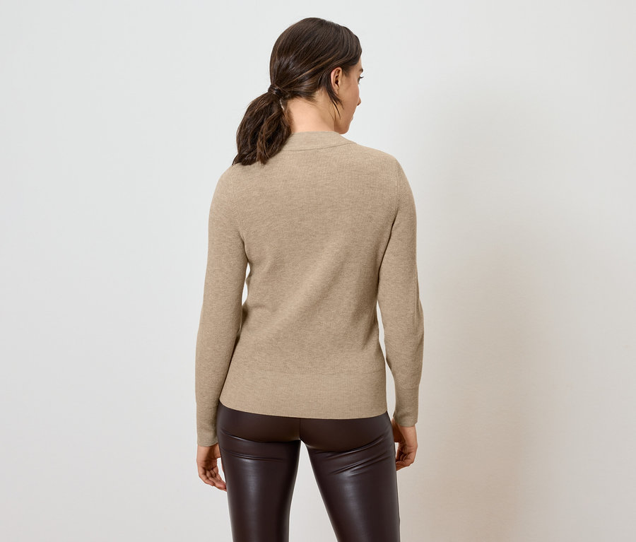 Frau mit dem Rücken zur Kamera trägt einen beigen Pullover und braune Lederhose.