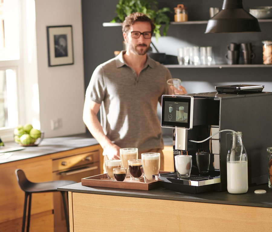 Mann hält Tasse neben »Tchibo Office« Kaffeevollautomat, schwarz.