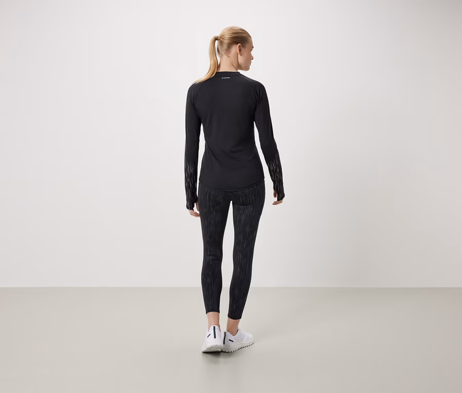 Eine Frau mit dem Rücken zur Kamera trägt ein schwarzes Langarmshirt und gemusterte Leggings.
