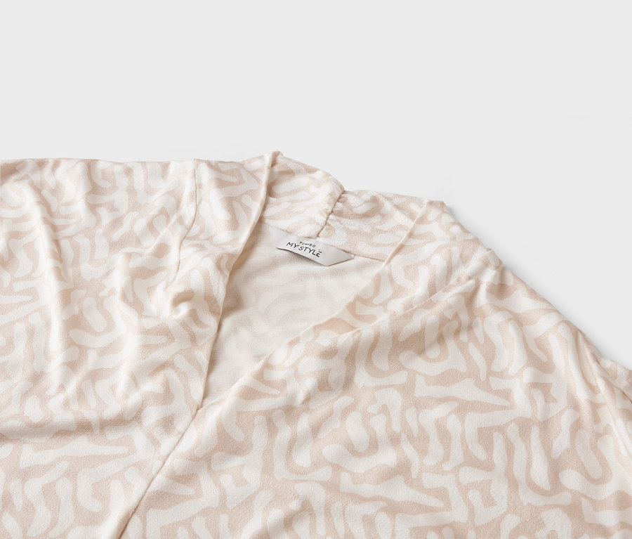 Nahaufnahme eines hellen Mantels mit abstraktem Muster und einem 'MY STYLE'-Etikett.