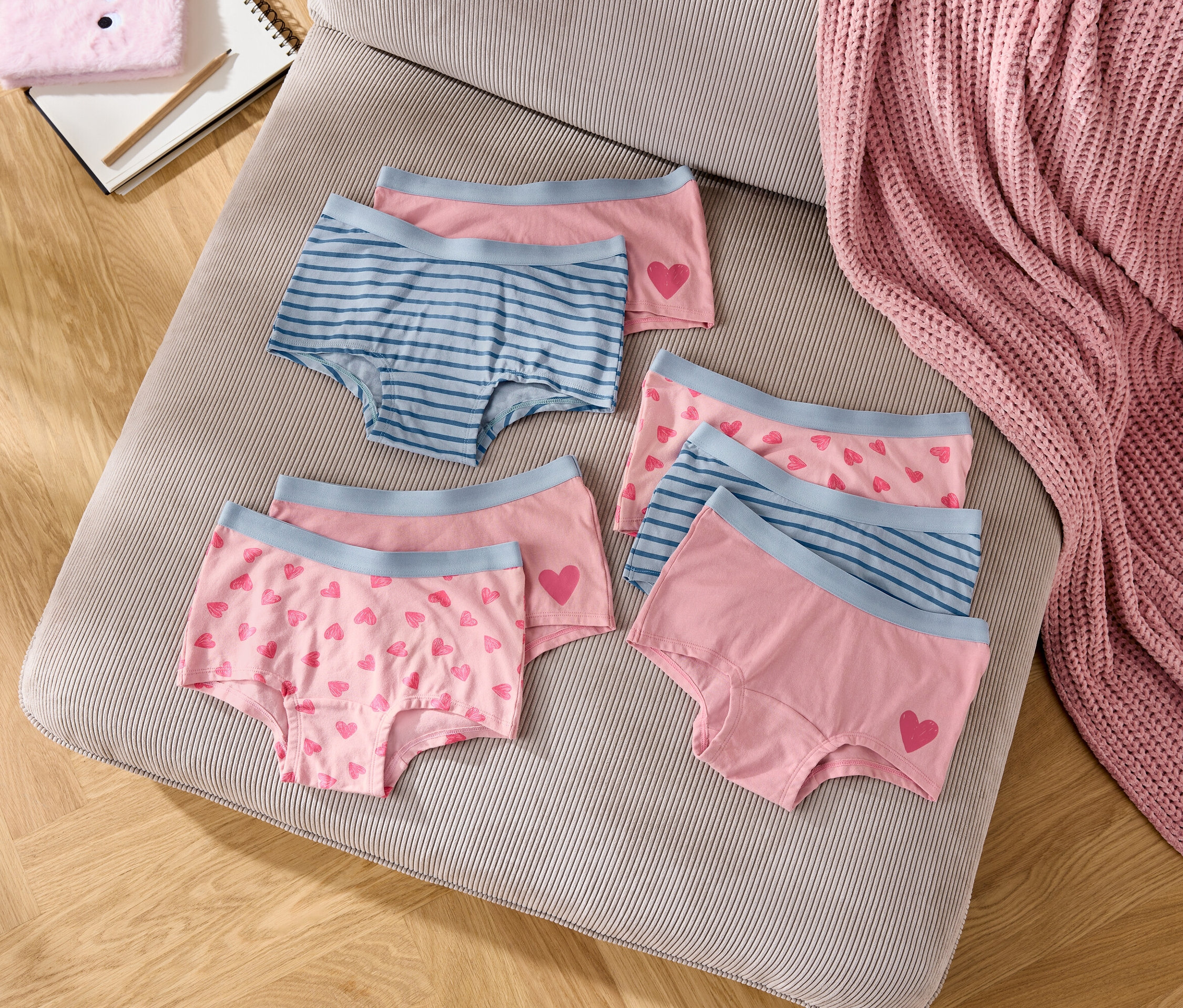 Auf einem gestreiften Kissen liegen sechs Mädchenslips in Rosa und Blau.