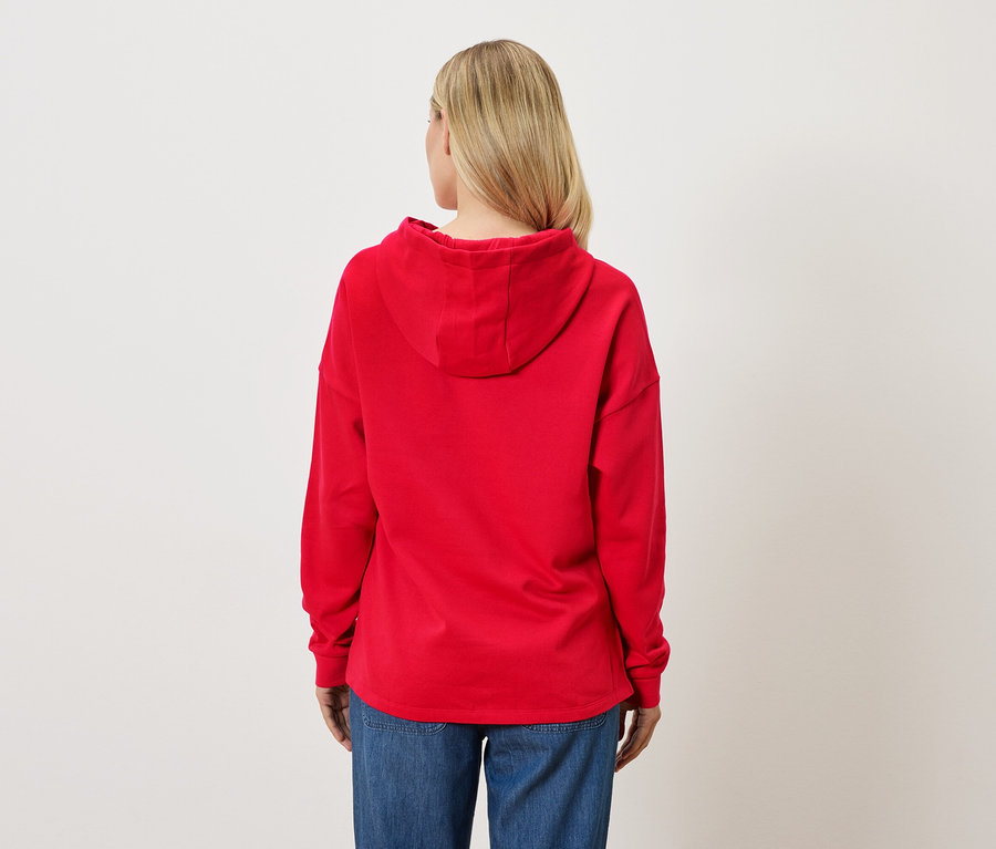 Rückansicht einer blonden Frau, die einen roten Hoodie und Jeans trägt.