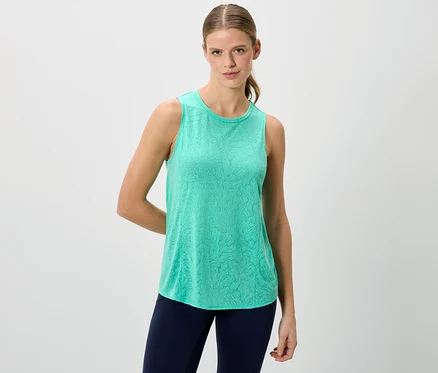 Frau trägt ein grünes Tanktop und blaue Leggings vor einem weißen Hintergrund.