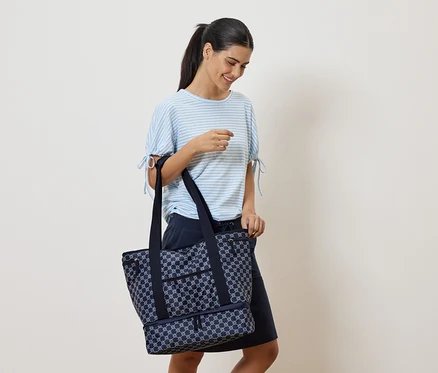 Lächelnde Frau mit blau-weiß gestreiftem Shirt und marineblauem Rock hält eine marineblaue Tragetasche mit Muster.