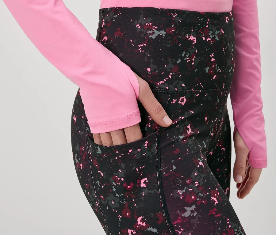 Frau mit pinkem Oberteil und gemusterter Leggings mit Tasche. Ihre Hand steckt in der Tasche.