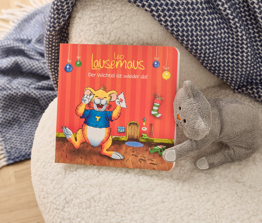 Auf einem weißen Hocker liegen ein Bilderbuch mit einem Cartoon-Löwen und ein graues Stofftier in Katzenform.