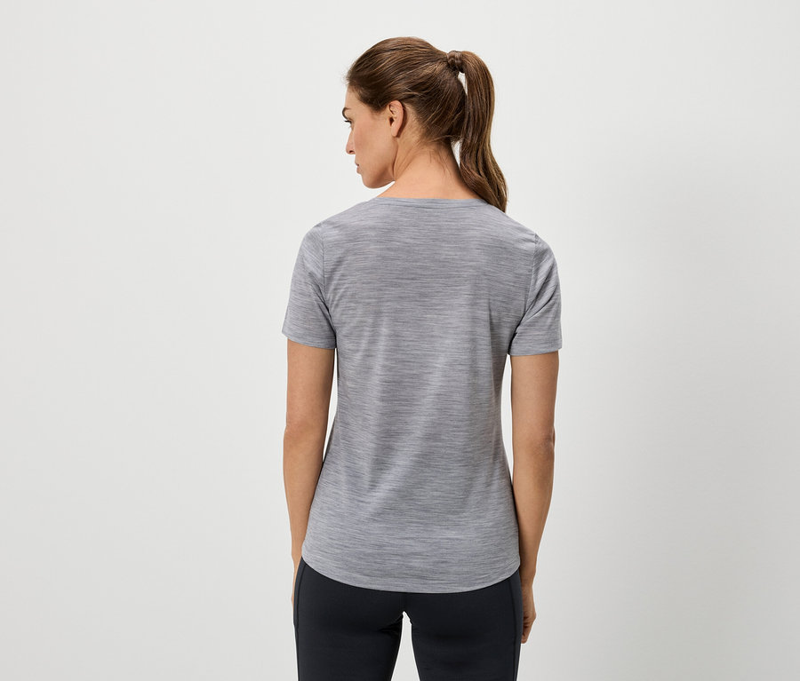 Rückansicht einer Frau mit Pferdeschwanz, die ein graues T-Shirt und eine dunkle Hose vor einem hellen Hintergrund trägt.