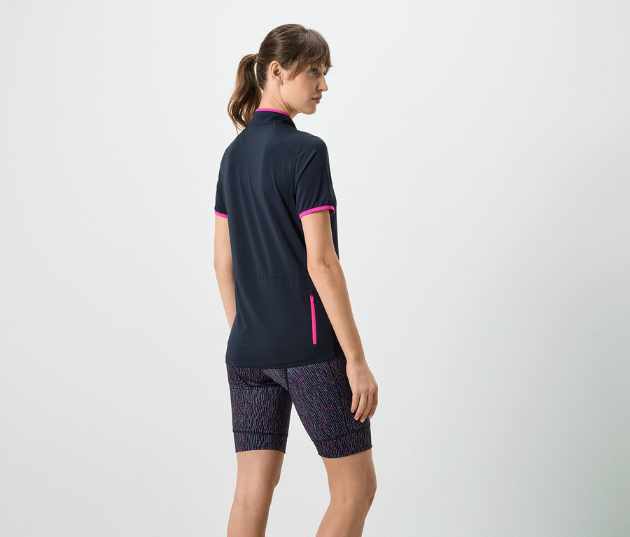 Frau von hinten, trägt ein marineblaues kurzärmeliges Shirt mit pinkfarbenen Akzenten und gemusterte Shorts.