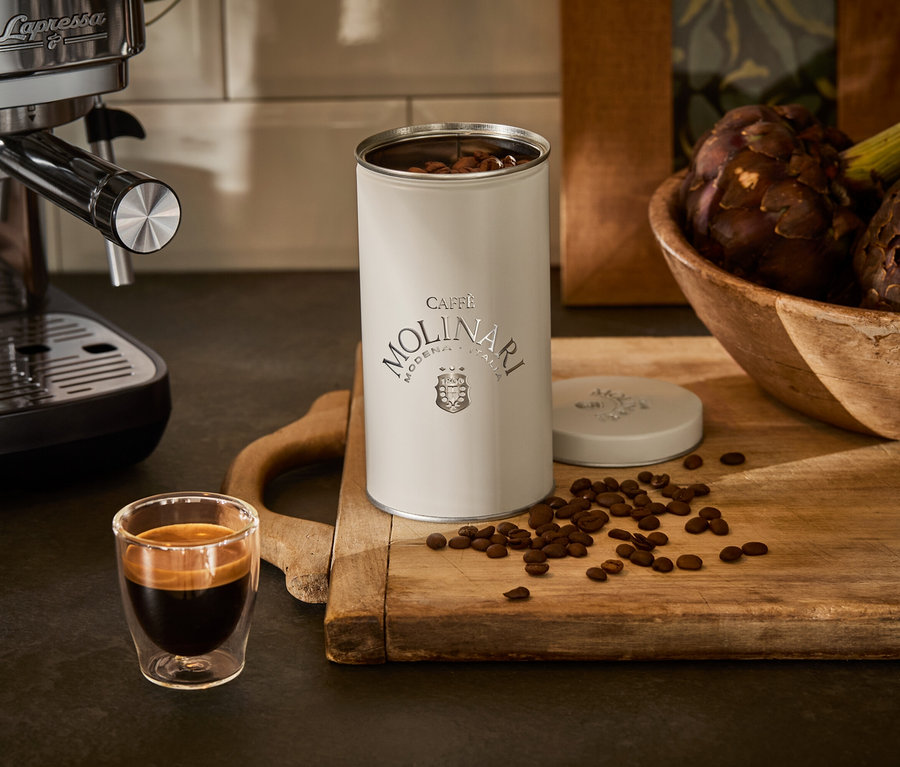 Espressomaschine neben Tasse und Caffe Molinari Dose auf einem Holzbrett.