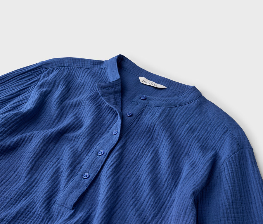 Nahaufnahme eines blauen, geknöpften Hemdes mit Stehkragen und langen Ärmeln.