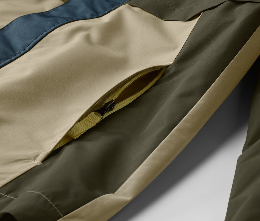 Nahaufnahme einer Jacke mit einer Reißverschlusstasche in Beige, Olivgrün und Blau.